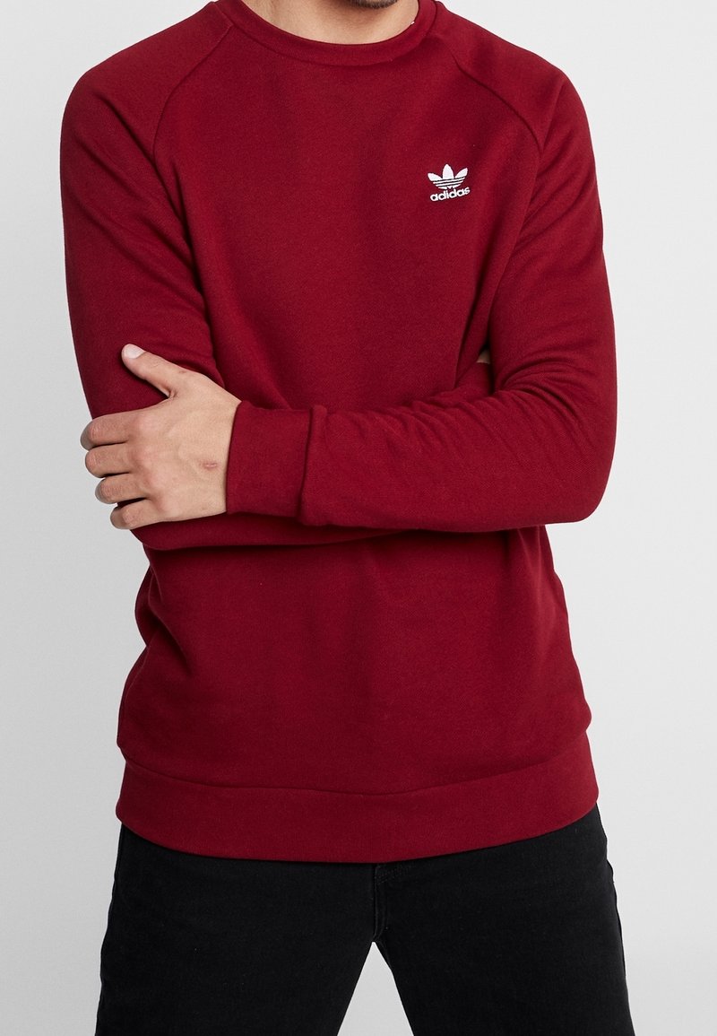 Bordeaux huppari, jossa on pyöreä kaula-aukko, resorit hihoissa ja helmassa. Vasemmassa rinnassa on valkoinen Adidas-logo. Pehmeää puuvillakangasta.