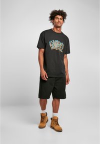 Sort bomulds t-shirt med farverig grafisk tekst på forsiden, parret med sorte shorts og beige arbejdssko med brune snørebånd.