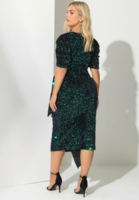 Mustapohjainen ja vihreä paljeteilla koristeltu mekko puffihihoilla, muotoiltu vyötärö ja korkeahko helma, yhdistettynä mustiin korkokenkiin.