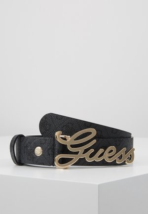 Czarny teksturowany pasek zwinięty na białej powierzchni z dużą, złotą metalową klamrą w kształcie logo "Guess" oraz małymi, okrągłymi metalowymi ćwiekami.