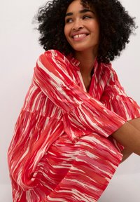 Robe à motifs rouge et blanc avec une coupe décontractée, un col mandarin et des manches longues. Le tissu semble léger avec une texture douce.