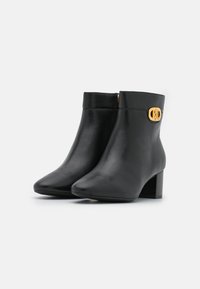 Botas de cuero negras hasta el tobillo con punta afilada, tacón bloque de altura media y acento dorado en el lado. Textura suave, diseño elegante.