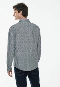 Grå mönstrad långärmad skjorta med en nedknäppt krage, textil med struktur och en rundad nederkant, kombinerad med mörkblå jeans.