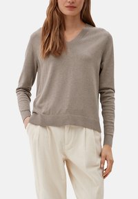 Pull à col en V en tissu tricoté taupe clair, doté de manches longues et d'un ourlet côtelé, associé à un pantalon plissé de couleur crème.