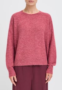 Maglione rosa a maglia con scollo rotondo, spalle basse e orlo a costine. Presenta una texture morbida e una vestibilità comoda.