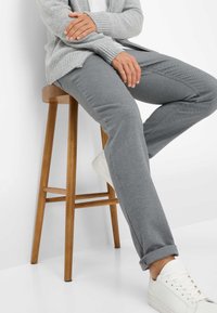 Grau strukturierte Hose mit geradem Schnitt und umgeschlagenen Säumen, kombiniert mit weißen Sneakers. Ein hellgrauer Cardigan wird über einem weißen Hemd getragen.