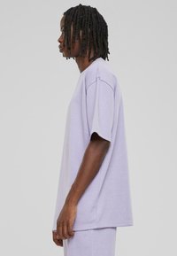 Helllila kurzärmliges T-Shirt mit lockerer Passform, Rundhalsausschnitt und weichem Material. Die Seitenansicht zeigt nahtlose Verarbeitung und überschnittene Schultern.