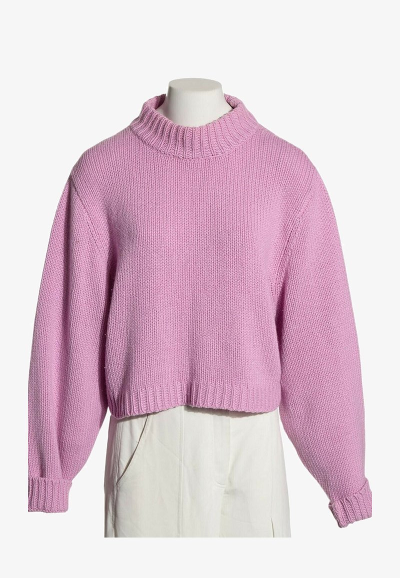 Pull court rose en maille avec manches longues et col, poignets et ourlet côtelés, présenté sur un mannequin portant un pantalon blanc.