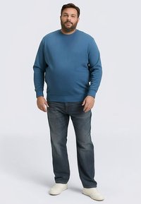 Blauwe trui met een ronde hals, geribde manchetten en zoom. Gecombineerd met donkerblauwe spijkerbroek en witte sneakers. Gladde stoftextuur.