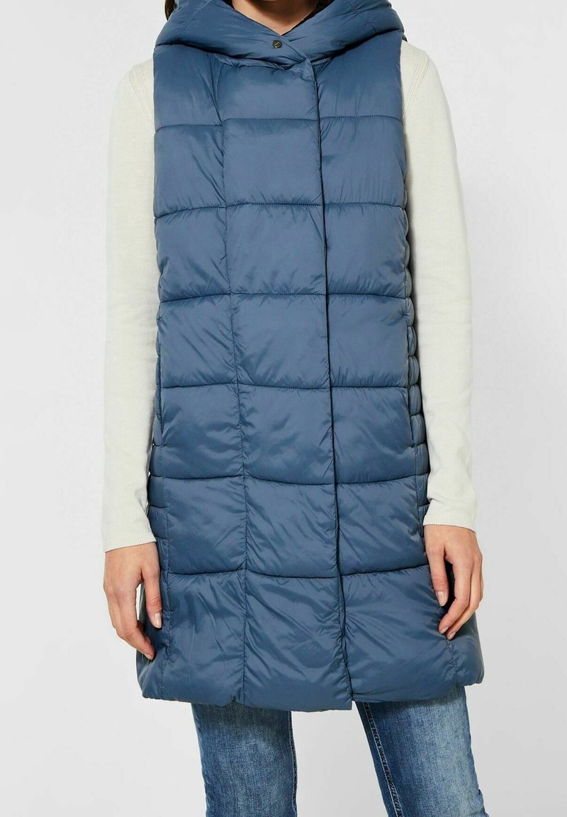 Vadderad marinblå väst med luva, med en quiltad design, framknäppning och sidofickor. Tillverkad av lätt, slät tyg.