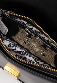 Interno di una borsa in pelle nera che mostra una tasca con zip e un dettaglio del logo argento. Foderato con tessuto bianco che presenta un motivo a scritta nera e una cerniera dorata.