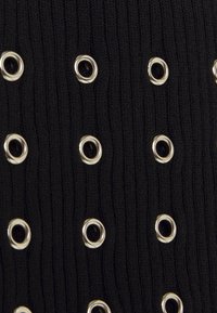 Schwarzer Strickstoff mit gleichmäßig verteilten silbernen Ösen, die dem Material Textur und ein Muster aus Löchern verleihen.