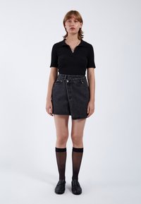Zwarte geribbelde polo met korte mouwen gecombineerd met een zwart denim rok met hoge taille, voorzien van een diagonale voorkantnaad en metalen knopen. Zwarte kniehoge sokken en loafers.