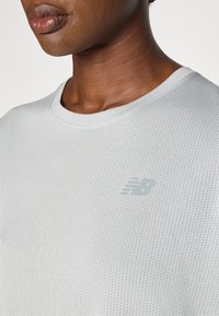 T-shirt de sport gris clair en tissu en mesh respirant, avec un col rond et une surface texturée ornée d'un petit logo.