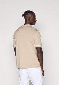 Šviesiai ruda polo marškinėliai trumpomis rankovėmis, su baltais dryželiais ant apykaklės ir rankovių, atsipalaidavusio kirpimo su šoninėmis skilčių detalėmis.