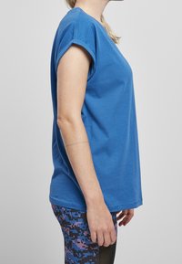 T-shirt blu a maniche corte in cotone con fit rilassato, scollo arrotondato e maniche arrotolate, abbinato a leggings a fantasia in viola e nero.