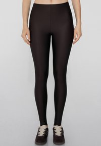 Leggings noirs en tissu lisse et extensible avec une taille haute. Présente un design ajusté s'étendant jusqu'à la cheville.