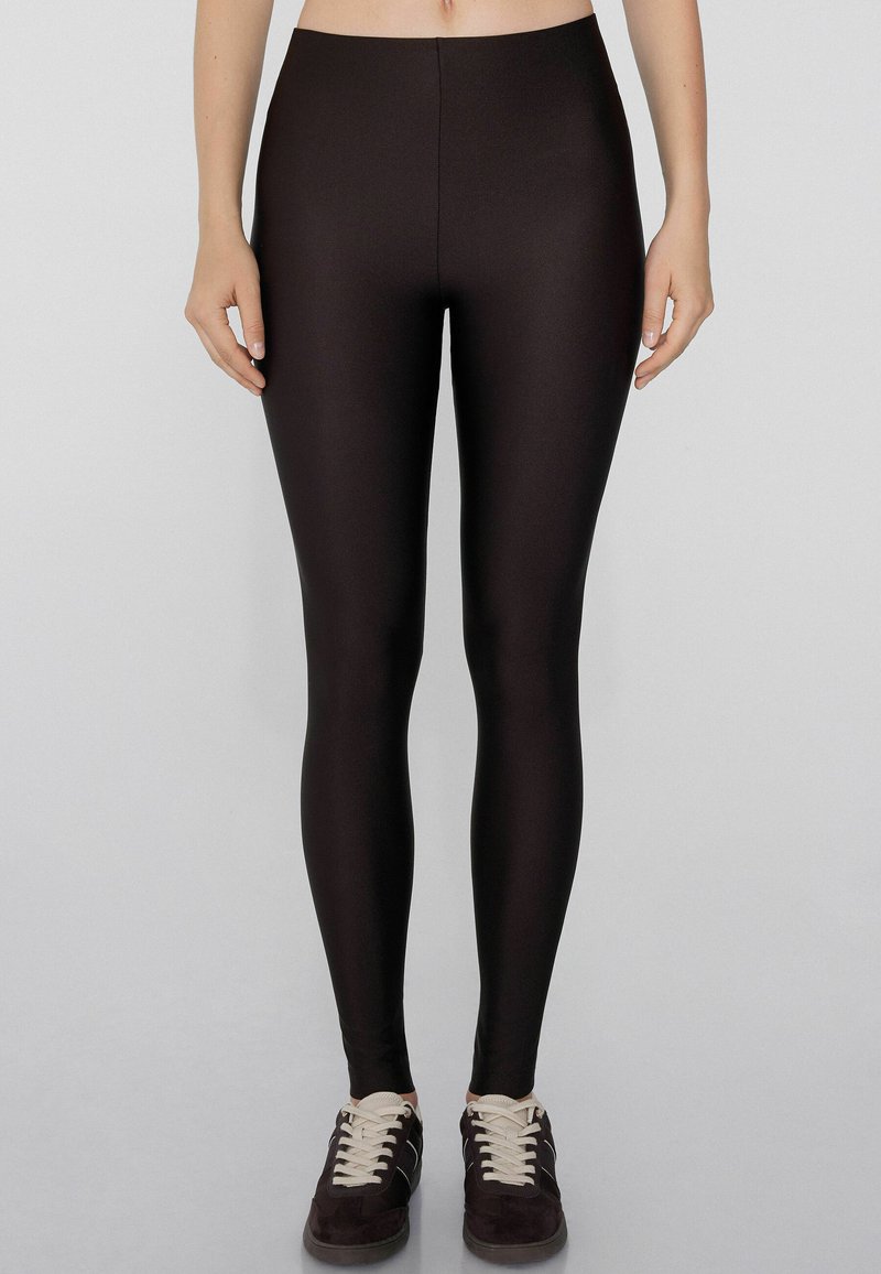 Leggings noirs en tissu lisse et extensible avec une taille haute. Présente un design ajusté s'étendant jusqu'à la cheville.