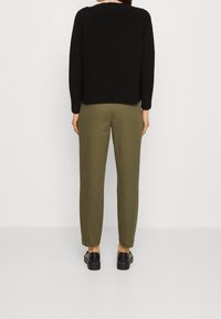 Svart stickad tröja med långa ärmar, kombinerad med olivgröna smala byxor och svarta platåskor. Enkelt design, inga synliga mönster.