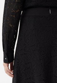 Schwarzes Spitzenkleid mit Paisley-Muster, langen Ärmeln und einem soliden Taillenband. Die Textur ist komplex und zart.