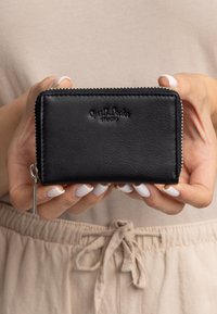 Schwarze Lederbörse mit strukturiertem Finish, ausgestattet mit einem Reißverschluss, geprägtem Logo auf der Vorderseite und einem Reißverschlusszug mit Silberverzierung.