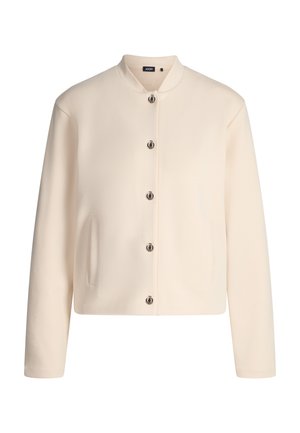 Veste couleur crème avec un col rond, des boutons argentés, deux poches latérales et une texture lisse. Design simple et droit.