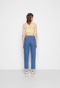 Zelený proužkovaný crop top, modré džíny s vysokým pasem, se zadními kapsami a rovnými nohavicemi, doplněný chunky béžovými teniskami.