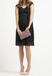 Mustasilkinen äitiysmekko, jossa on lyhyet hihat, määritelty vyötärö ja aaltoileva helma, yhdistettynä vaaleanpunaiseen clutch-laukkuun ja nude-korkokenkiin.