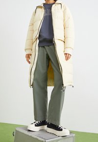 Abrigo acolchado crema con cierre de cremallera, combinado con un sudadera azul marino y pantalones verde olivo. Zapatillas de plataforma negras con suelas blancas.