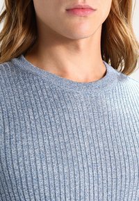 Pull en rib avec une teinte bleu clair, à col rond classique, fabriqué à partir d'un tissu tricoté texturé, présentant des variations subtiles de ton.