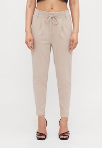 Beżowe zwężane spodnie z paskiem na sznurku, plisowanym przodem i gładkiego materiału. Połączone z czarnymi sandałami na wysokim obcasie z paskami.