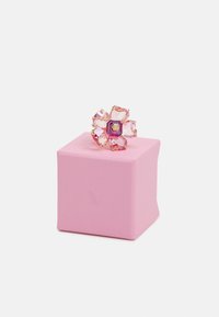 Anillo floral hecho de cristales rosas, con un diseño de múltiples pétalos y un centro púrpura, descansando sobre una caja de regalo rosa texturizada.