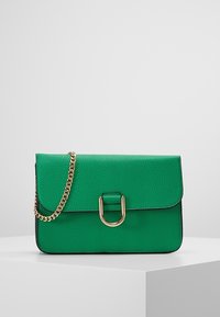 Grön texturerad handväska med ett guldkedjesnör, en strukturerad form, lockstängning och en cirkulär hårdvaruaccent på framsidan.