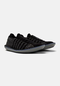 Black athletic shoes with a textured knit upper, featuring black laces and a low-profile gray rubber sole. Striped pattern on sides.