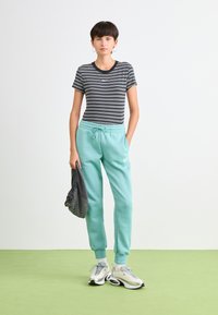 Svart- og hvitstripet t-skjorte med rund hals, kombinert med lyse tealfargede joggingbukser med elastisk midjebånd og logo. Hvite sneakers.