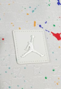 Bela teksturirana tkanina s barvnimi madeži barve. Ima dvignjen beli logotip Jumpman z obrobo iz šiva.