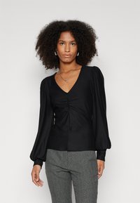 Black long-sleeve top with a V-neck, featuring gathered detailing at the center. Smooth fabric with slightly puffed sleeves, fitted silhouette.