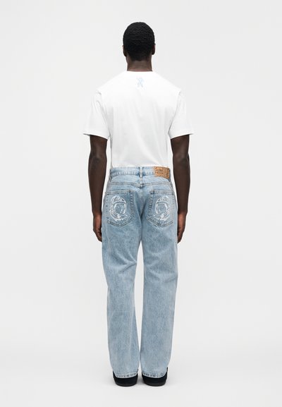 Λευκό t-shirt συνδυασμένο με ανοιχτό μπλε, φαρδιά τζιν με γραφικό αστροναύτη στις πίσω τσέπες και δερμάτινο ταμπελάκι στη μέση.