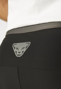 Zwarte leggings met een gladde textuur, voorzien van een grijs driehoekig logo van een leeuwen gezicht op de achterkant van de tailleband. Aangevuld met een grijze paneel.