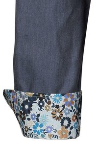 Jeans mit umgeschlagenem Saum und floralem Druck, der blaue, schwarze und braune Blumen vor einem hellen Hintergrund zeigt.