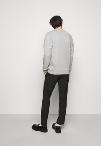 Sudadera gris con cuello redondo, combinada con pantalones negros y zapatos negros de suela gruesa. Diseño liso, sin patrones ni acentos visibles.