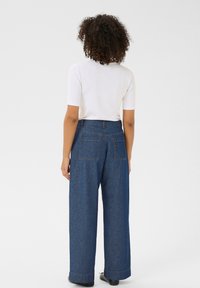 Pantalons en denim à jambes larges avec une finition bleu foncé, dotés de poches arrière et d'une taille haute. Associés à un haut blanc ajusté à manches courtes.