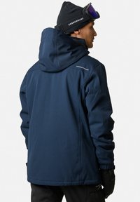 Navy blue waterproof jacket with a hood, featuring visible seams, adjustable cuffs, and a logo detail on the shoulder. Textured fabric.