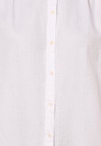 White button-up shirt made of lightweight fabric featuring a textured finish and pearl-colored buttons along the front.