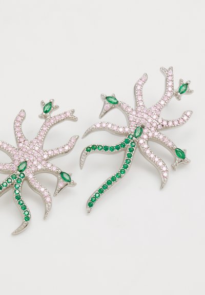 Silversmycken formade som havskreaturer, med rosa och gröna ädelstenar, och detaljerade intrikata mönster och svängande slingor.