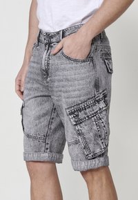 Shorts cargo en denim gris avec une finition usée, comportant des revers roulés, plusieurs poches et des détails de couture contrastants.