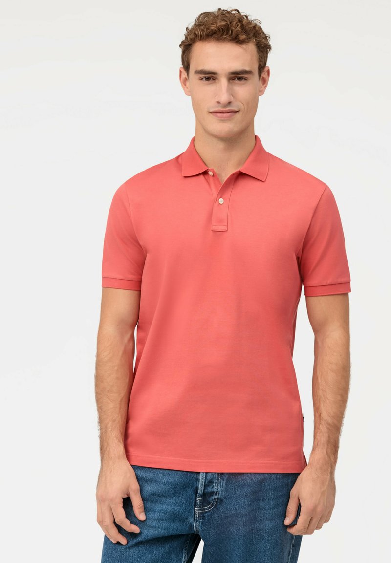 Polo en coton lisse couleur corail, avec un col et des manches courtes. Le polo a un léger brillant et une coupe classique.
