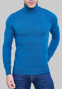 Pull à col roulé bleu en maille lisse, coupe ajustée, manches longues, poignets et ourlet côtelés, assorti avec un jean foncé.