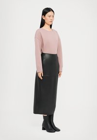Pulover roz deschis cu umeri căzuți, asociat cu o fustă midi din piele neagră. Botine negre până la gleznă completează ținuta. Texturi netede și design structurat.