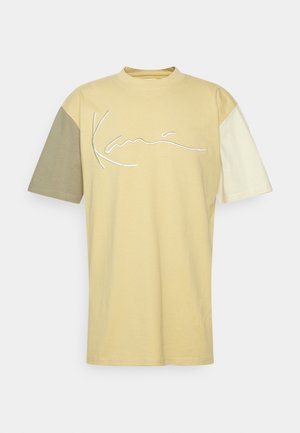 Kortærmet t-shirt med rund hals, med en gul krop, ærmer i grøn og cremefarvet, og hvidt broderet tekstlogo.